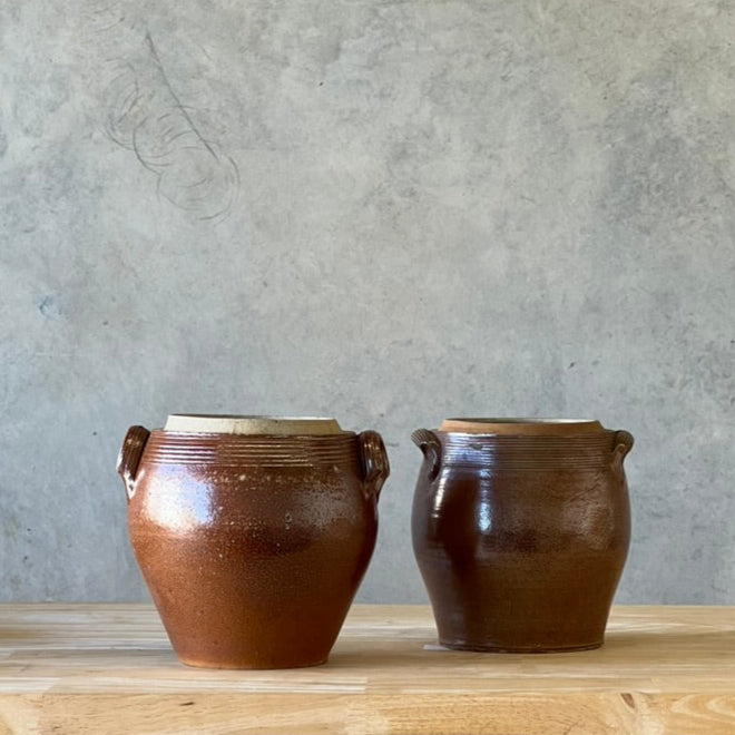 Two brown ceramic pots on a wooden surface with a gray wall background