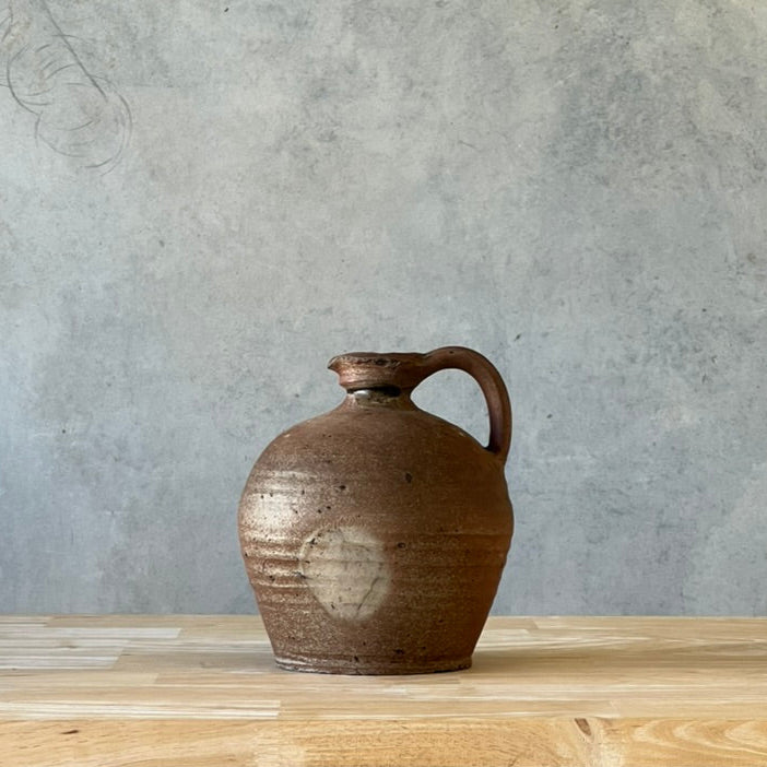 Brown ceramic jug on a wooden surface with a gray concrete wall background