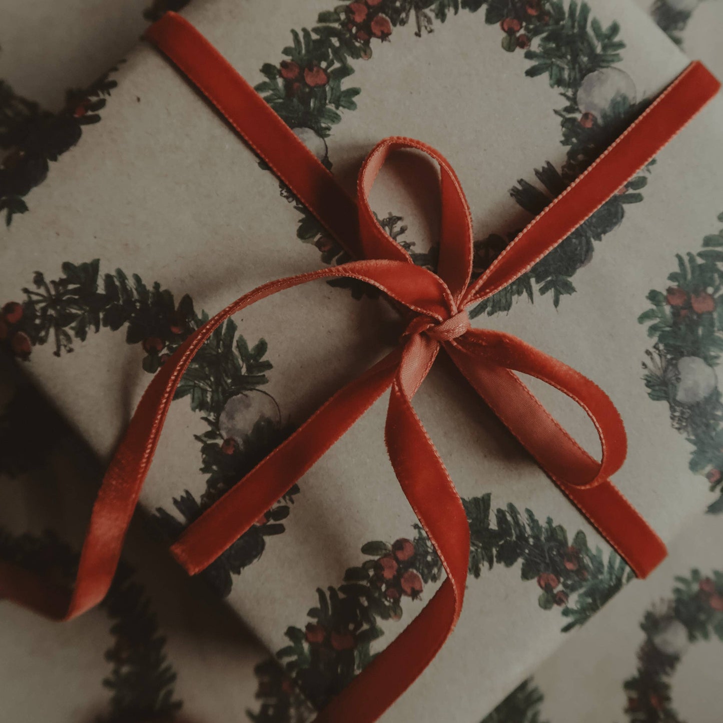Gift wrapped in paper with a festive christmas wreath design and red ribbon