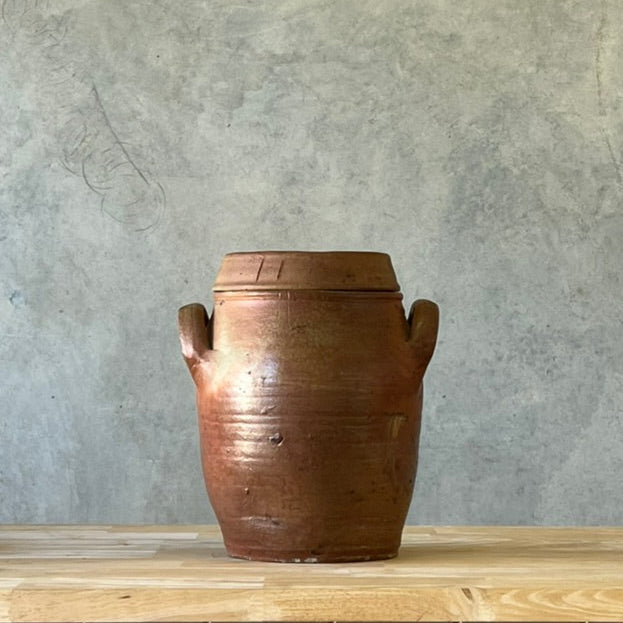Brown ceramic jar on a wooden surface with a gray concrete wall background