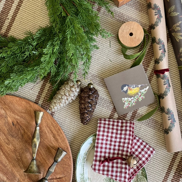 Decorative table setting with greenery, ornaments, and gift wrap on a textured surface.
