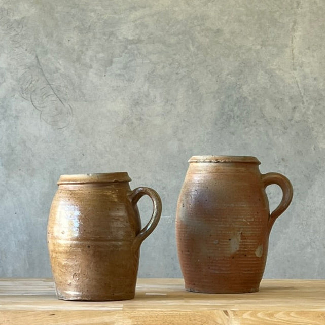 Two ceramic jars on a wooden surface with a gray wall background