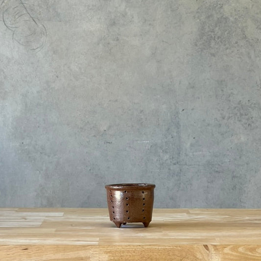 Brown ceramic pot on a wooden table with a gray concrete wall background