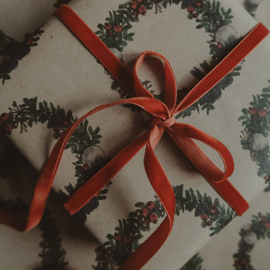 Gift wrapped in paper with a festive christmas wreath design and red ribbon