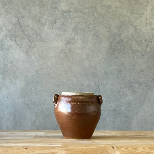 Brown ceramic vase on a wooden surface with a gray wall background