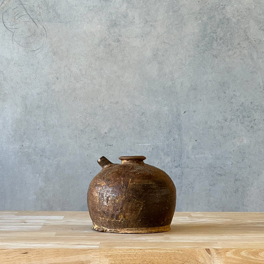 Brown ceramic pot on a wooden surface with a gray concrete wall background