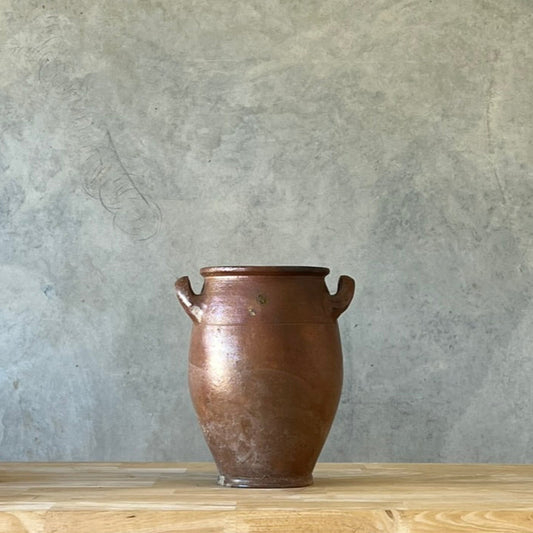 Antique French confit pot on a wooden surface with a gray wall background.