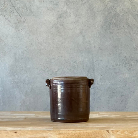 Brown ceramic pot on a wooden surface with a gray concrete wall background