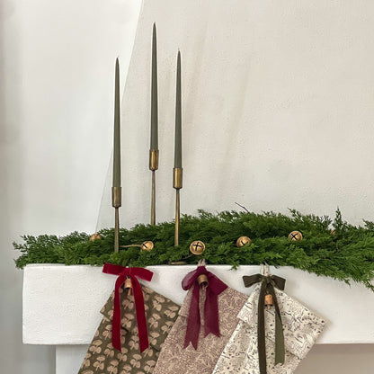 Decorative stockings hanging on a mantel with greenery and candles.
