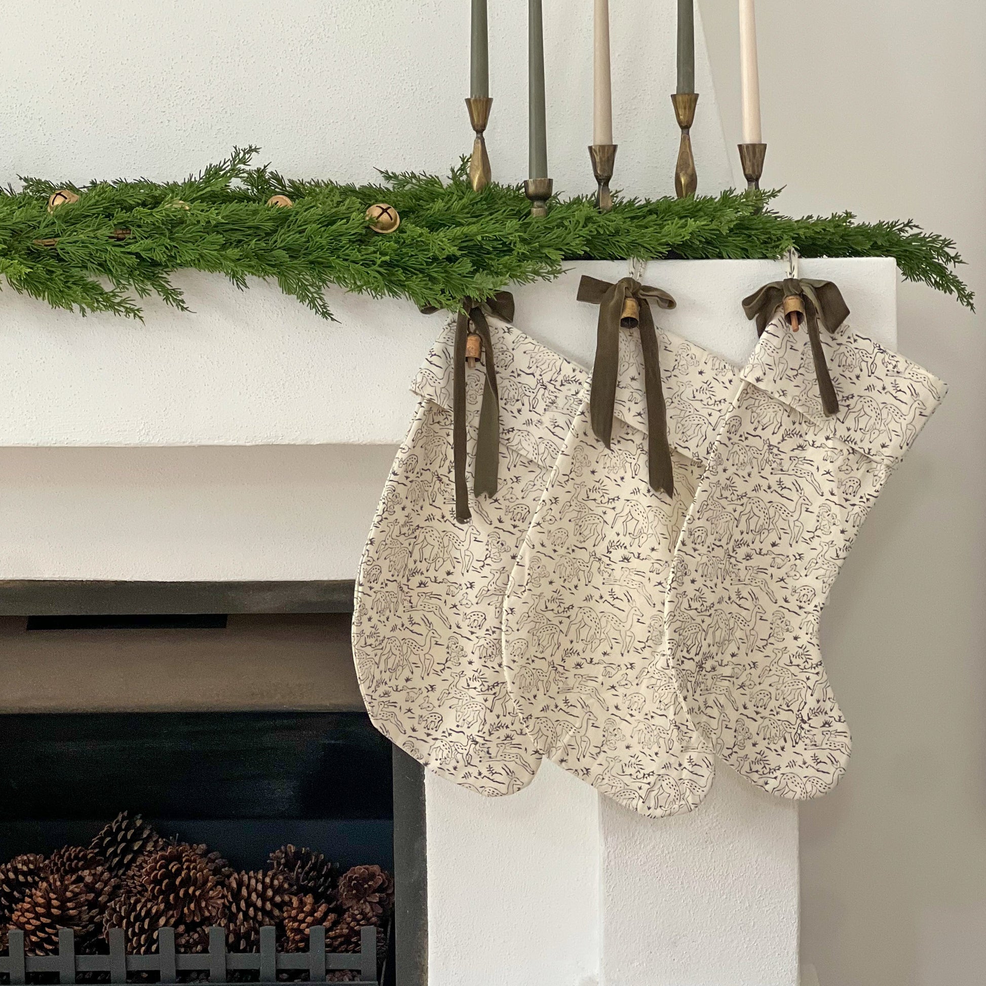 Decorative stockings hanging on a fireplace mantel with greenery and candles.