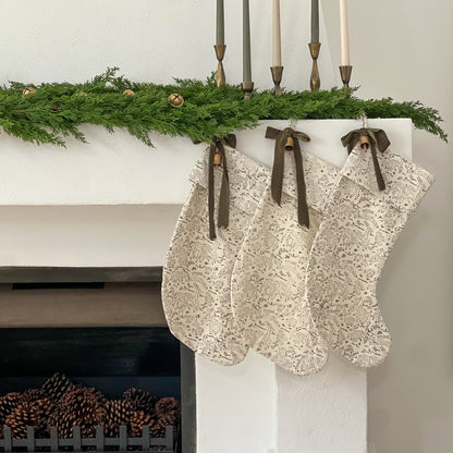 Decorative stockings hanging on a fireplace mantel with greenery and candles.
