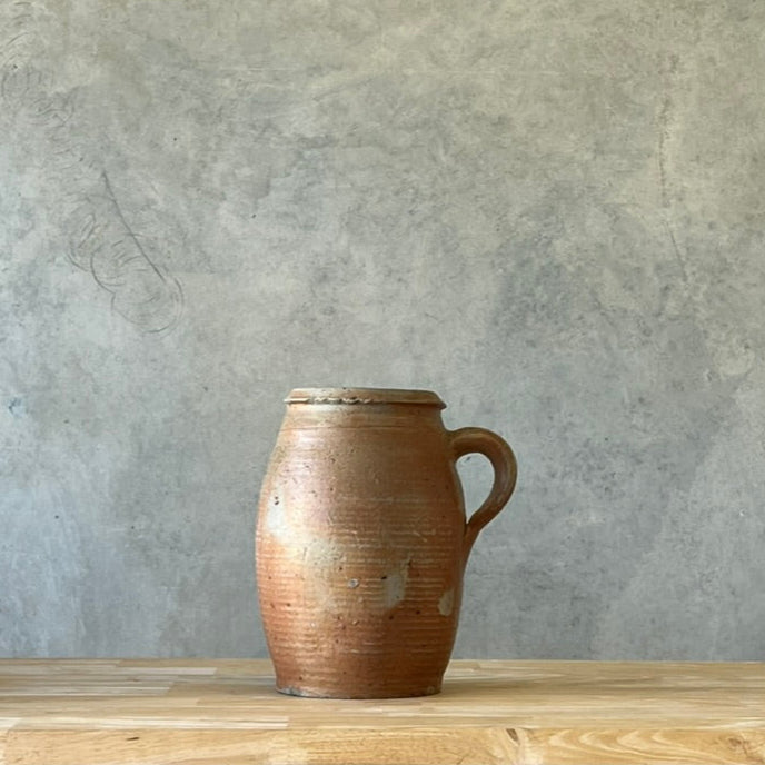 Brown ceramic pitcher on a wooden surface with a gray textured wall background