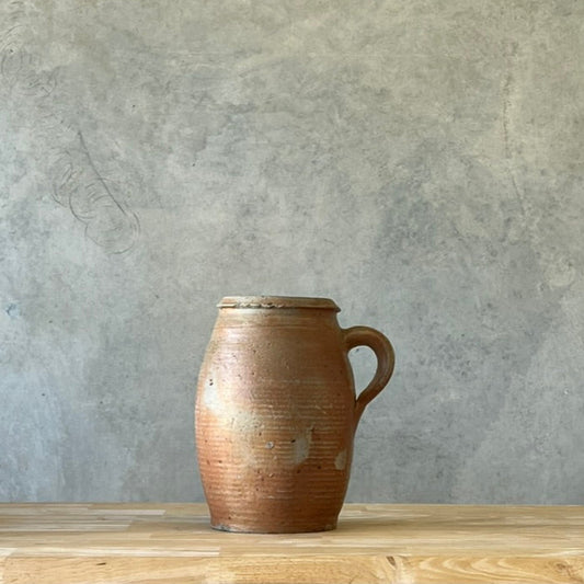 Brown ceramic pitcher on a wooden surface with a gray textured wall background